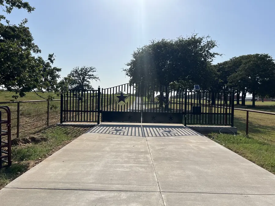 Black iron ranch entry gate with Texas star panels on a concrete drive