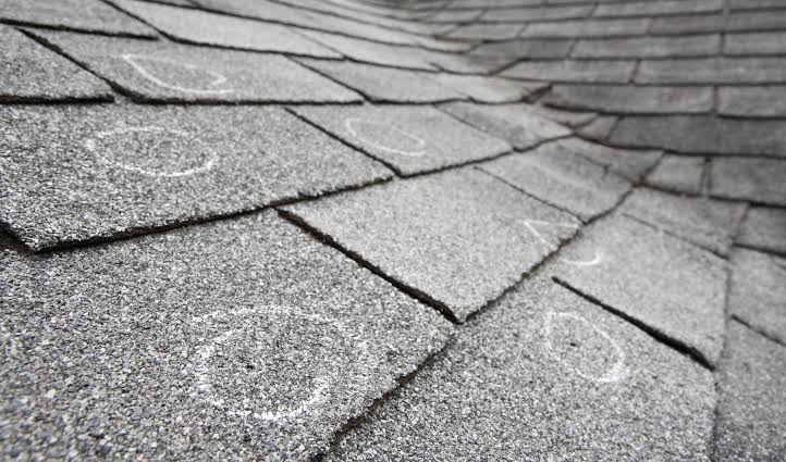 Close-up of hail bruising on an asphalt shingle showing granule loss and a fractured mat